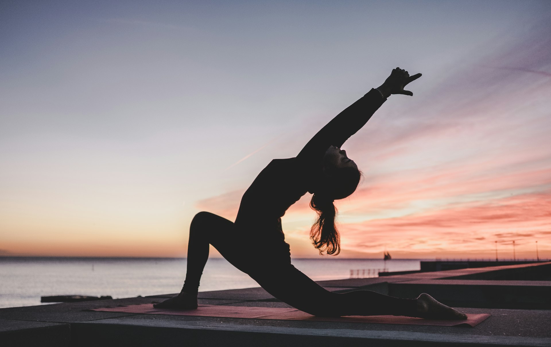 Silhouette of a woman in a yoga pose on a pier at sunset over the ocean